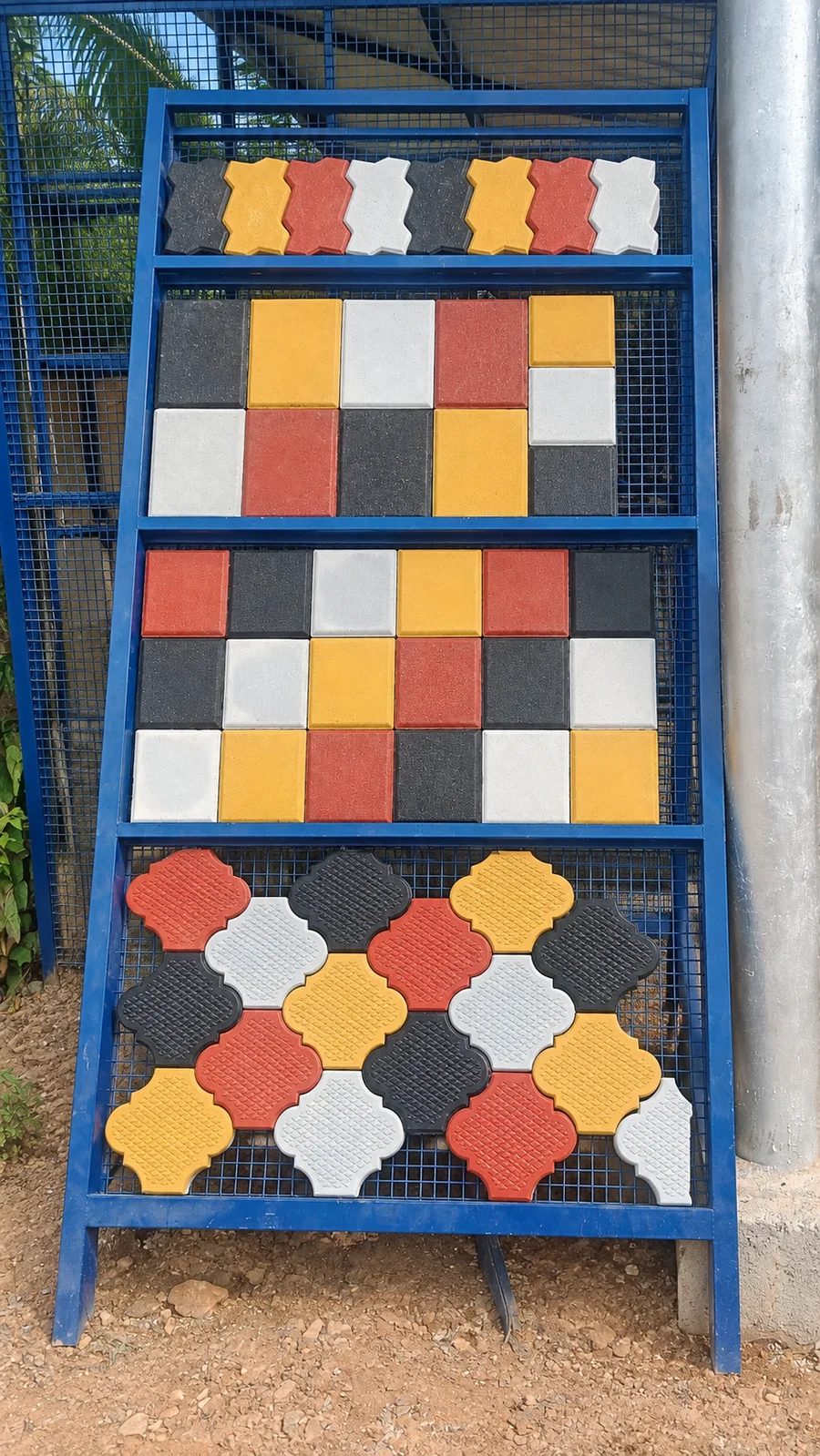 Sharavathi concrete paver samples in yellow, red, white and charcoal on a blue display rack